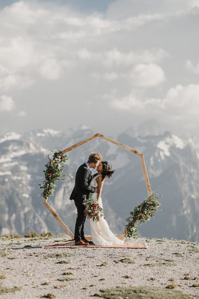 Elopement Brautpaar unter Blumenbogen auf einer Bergspitze mit Panoramablick