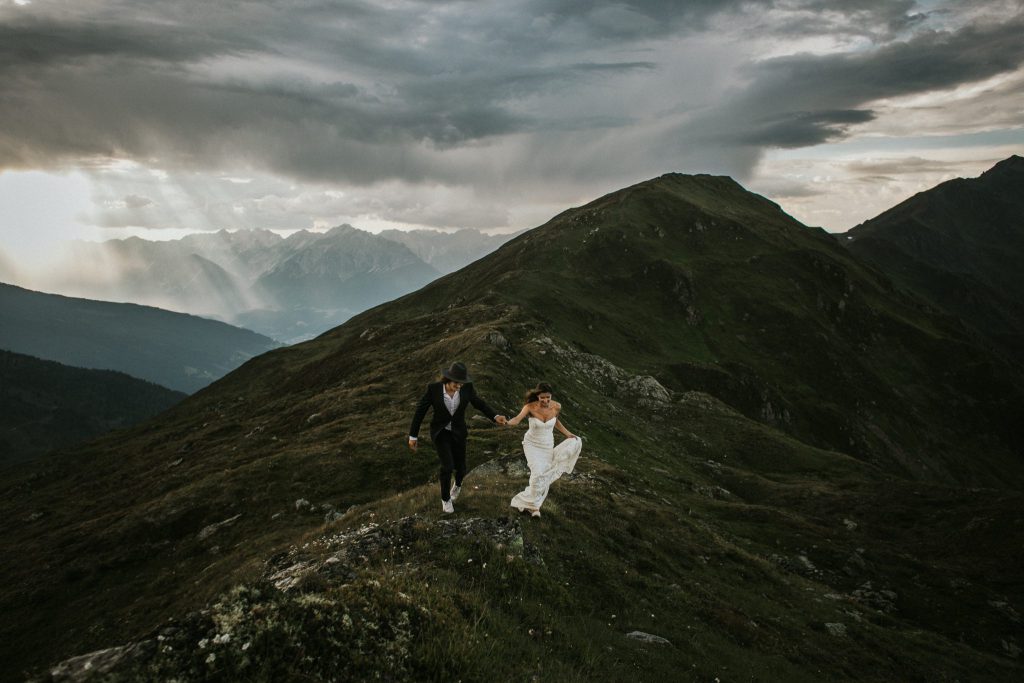Elopement: Rennendes Brautpaar auf einer Bergspitze in den Alpen