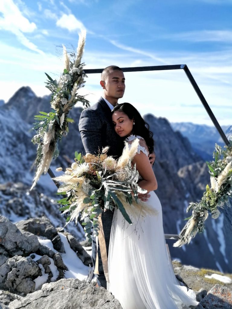 Elopement Brautpaar unter Blumenbogen auf einer Bergspitze mit Panoramablick